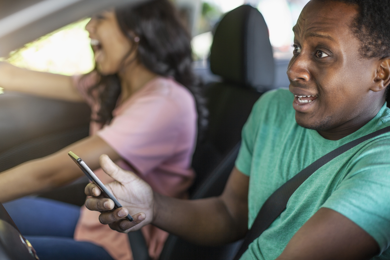 Young Black ethnicity teenager boy using holding smart phone while driving in car wearing seat belt distracted car accident crash