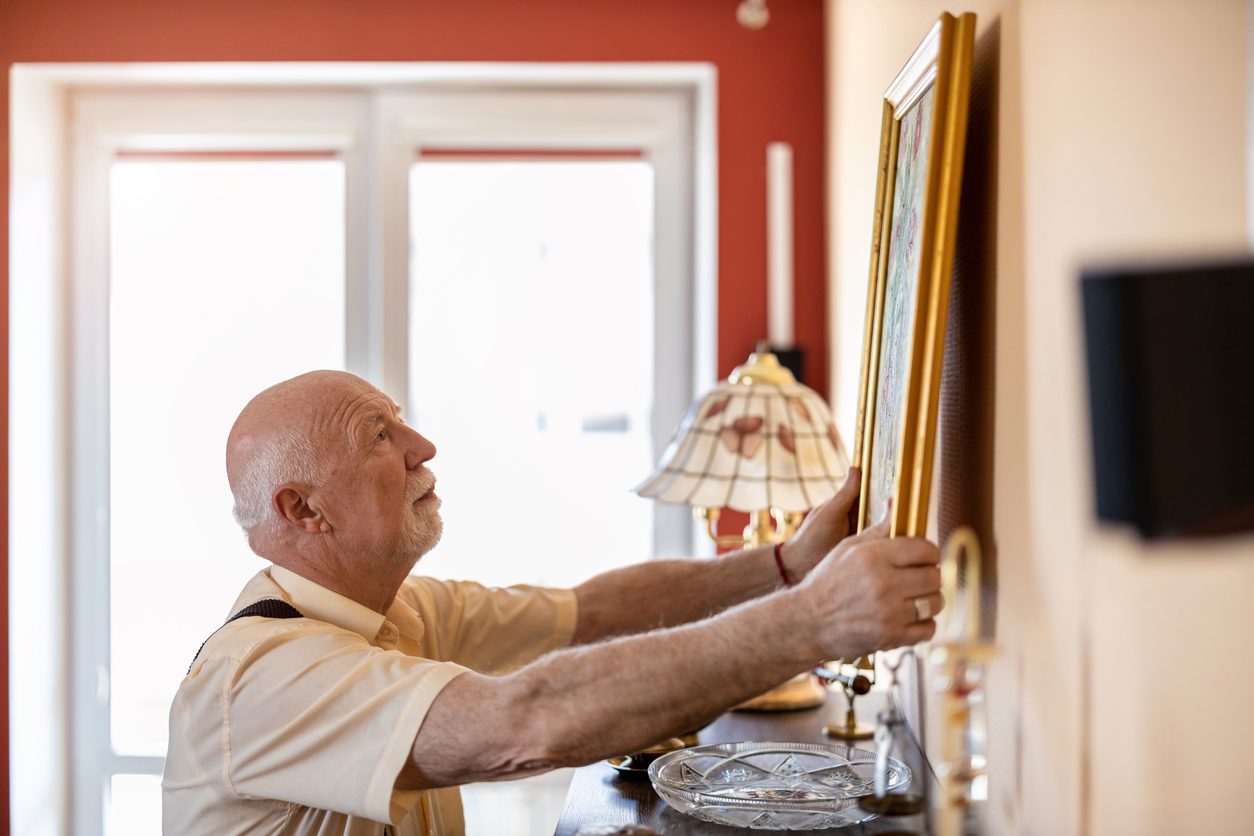 Senior man putting up a painting on the wall at his home