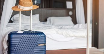 Blue-Luggage-with-hat-in-modern-hotel-room-after-door-opening.-Time-to-travel,-service,-journey,-trip,-summer-holiday-and-vacation-concepts
