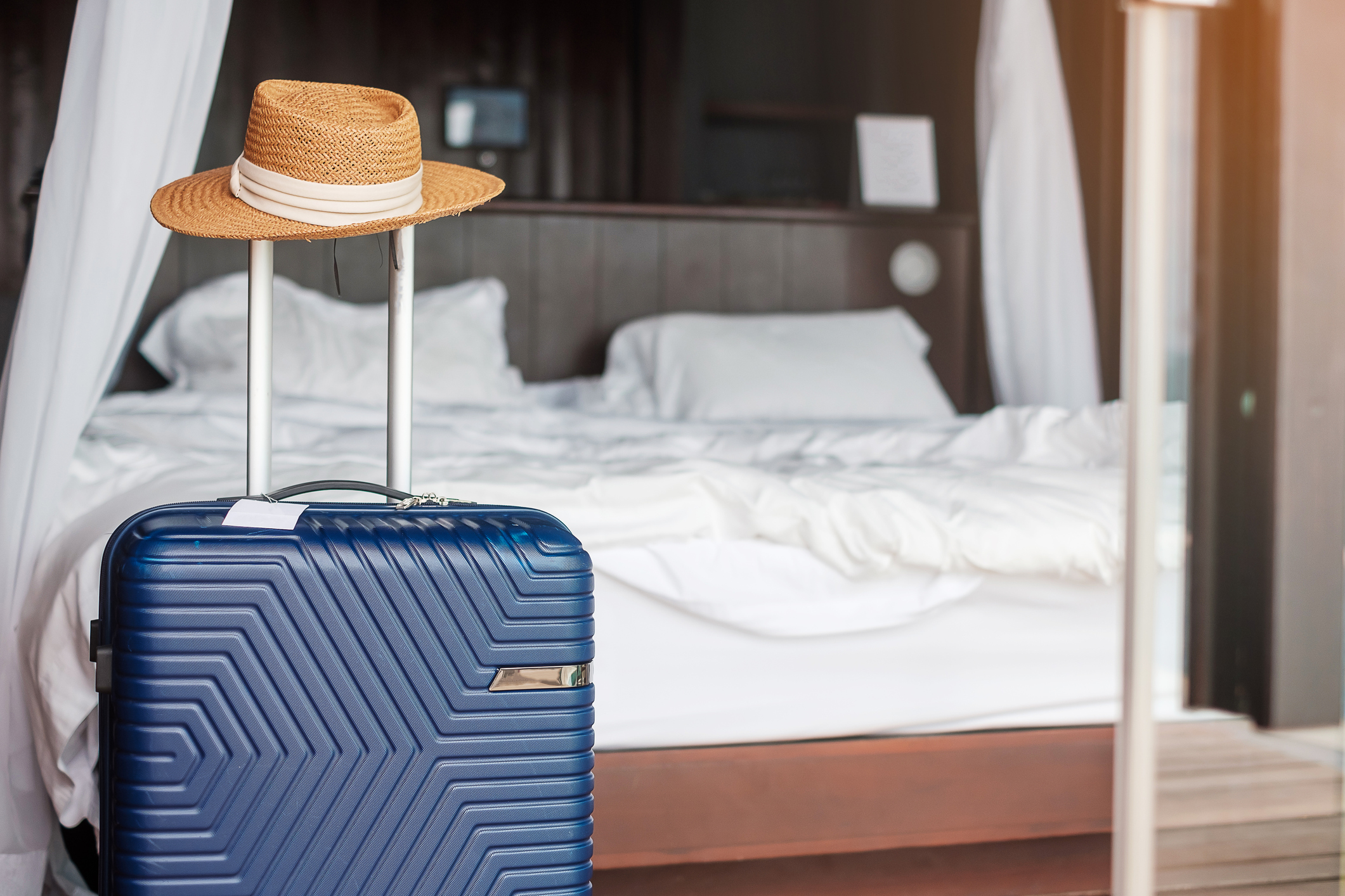 Blue-Luggage-with-hat-in-modern-hotel-room-after-door-opening.-Time-to-travel,-service,-journey,-trip,-summer-holiday-and-vacation-concepts