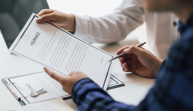 Man in office showing an insurance policy and pointing with a pen where the policyholder must to sign. Insurance agent man presentation and consulting insurance terms detail to customer and waiting for his signing.