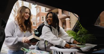 Two happy young women students loading belongings into car trunk for college move