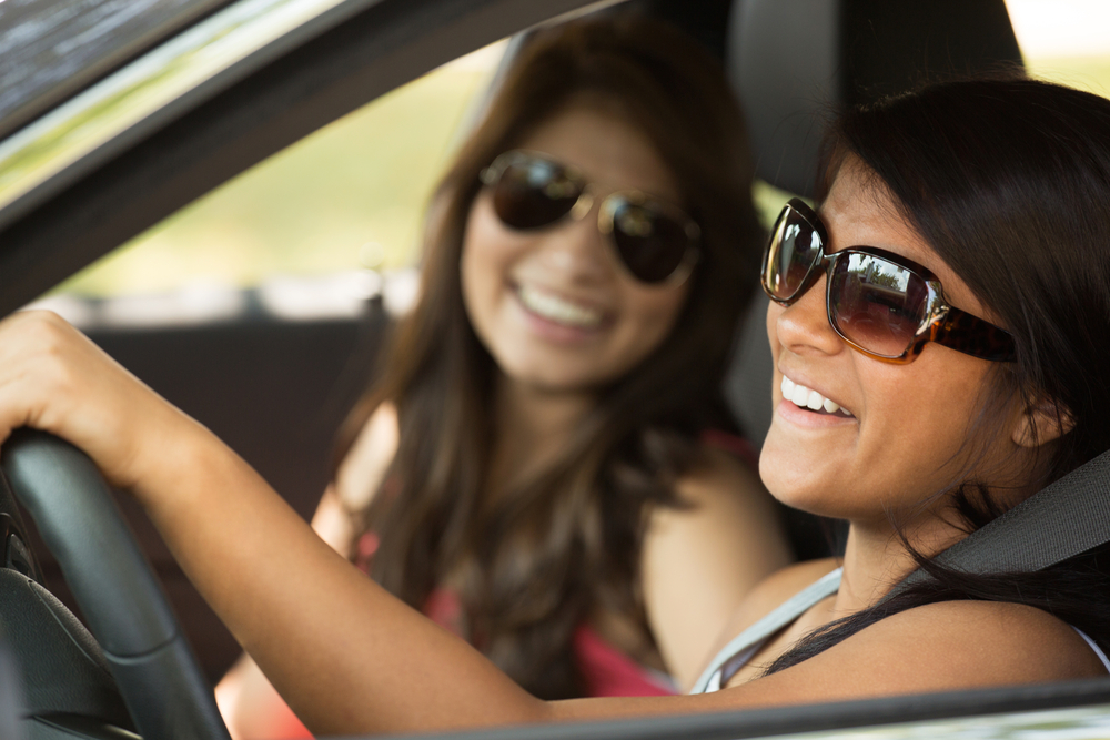 Two women wearing sunglasses are driving a car, enjoying a sunny day on the road.