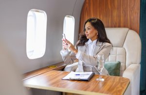 woman in a tan suit with dark hair sits in a chair on a private plane